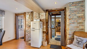 A room with a wooden floor, a white refrigerator, a wicker chair, and a brick wall.