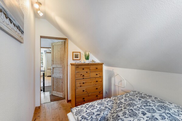 Ein Schlafzimmer mit einem Holzkoffer, einem Bett mit gemusterten Betttextilien, einem weißen Heizkörper und einer Tür zu einem anderen Raum.