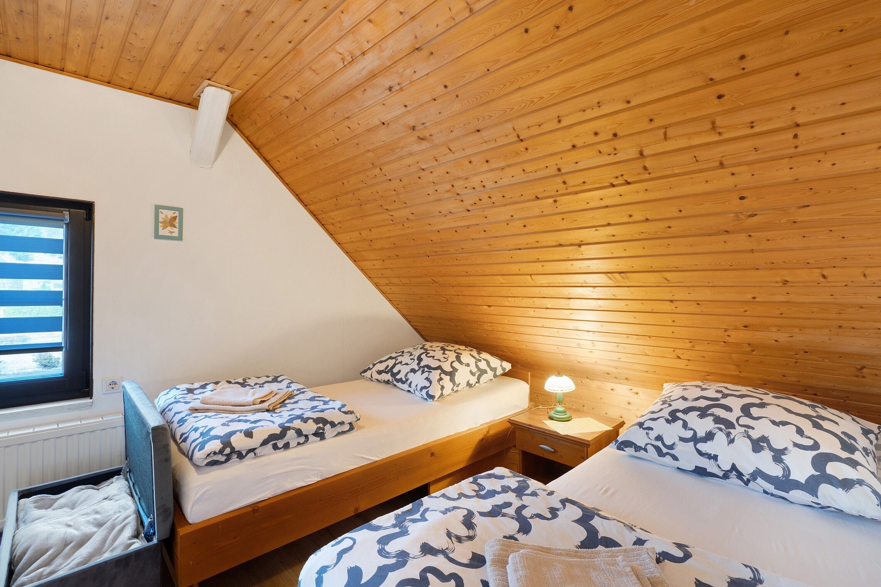 Ein Schlafzimmer mit zwei Betten, Holzboden, einem Fenster und einem Nachttisch mit Lampe.