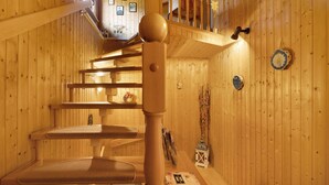 Un intérieur en bois avec un escalier, une chaise en bois et une petite table sur laquelle se trouve une lampe.
