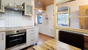 Une cuisine équipée d’un four encastré, de meubles blancs, d’un plan de travail en bois et d’une fenêtre donnant sur l’extérieur.