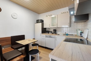 A compact kitchen with a microwave, coffee maker, and a dishwasher. There is a wooden table with two chairs and a bench.