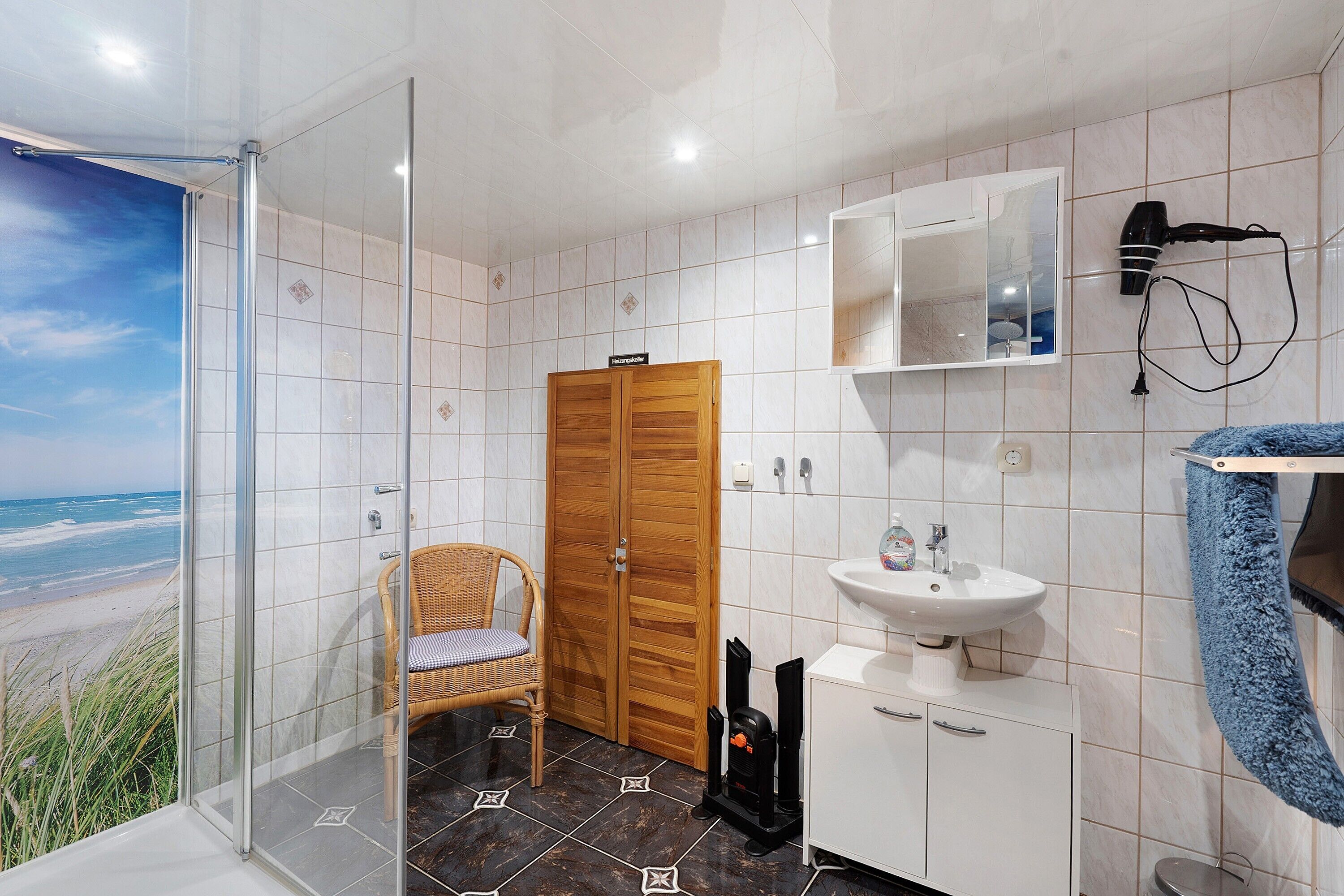 Een badkamer met een glazen douchecabine, een houten deur, een wit wastafelmeubel, een spiegel en een handdoekhouder.