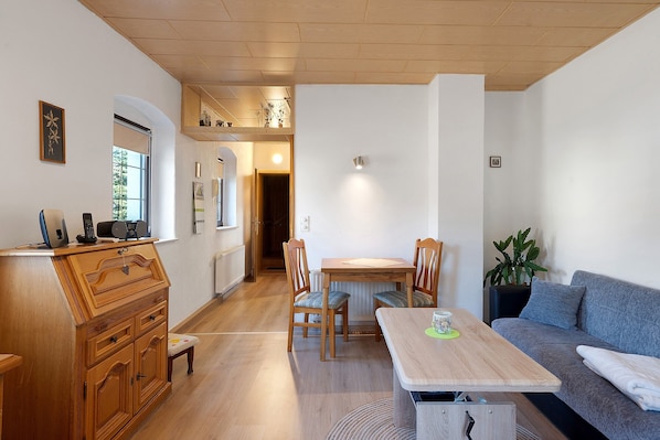 A room with a wooden dresser, a dining table with chairs, a sofa, and a potted plant.