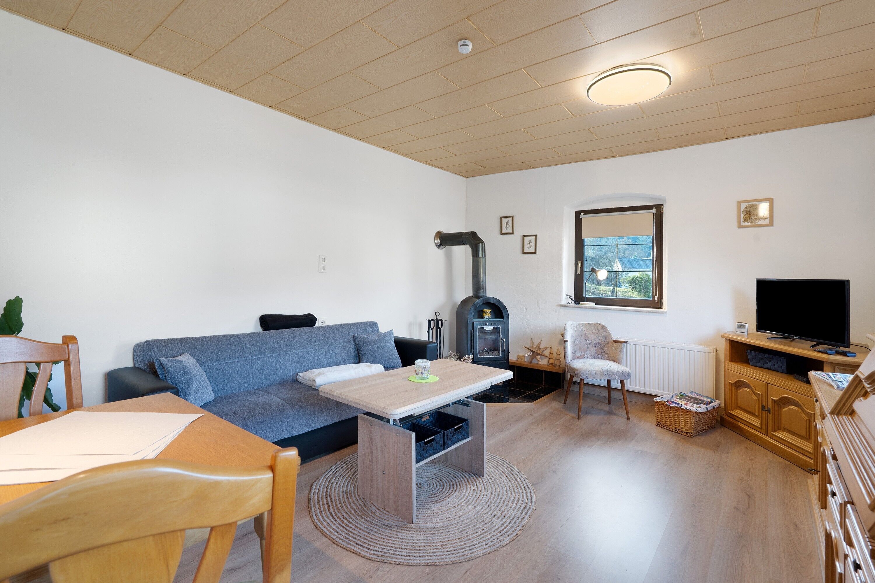 Una sala de estar con sofá, mesa, televisor, chimenea y ventana.