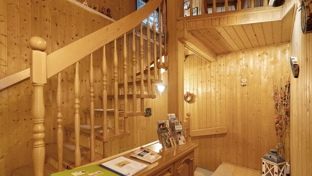 Un intérieur en bois avec un escalier, des murs en bois, un comptoir d’accueil avec des brochures et une petite lanterne.