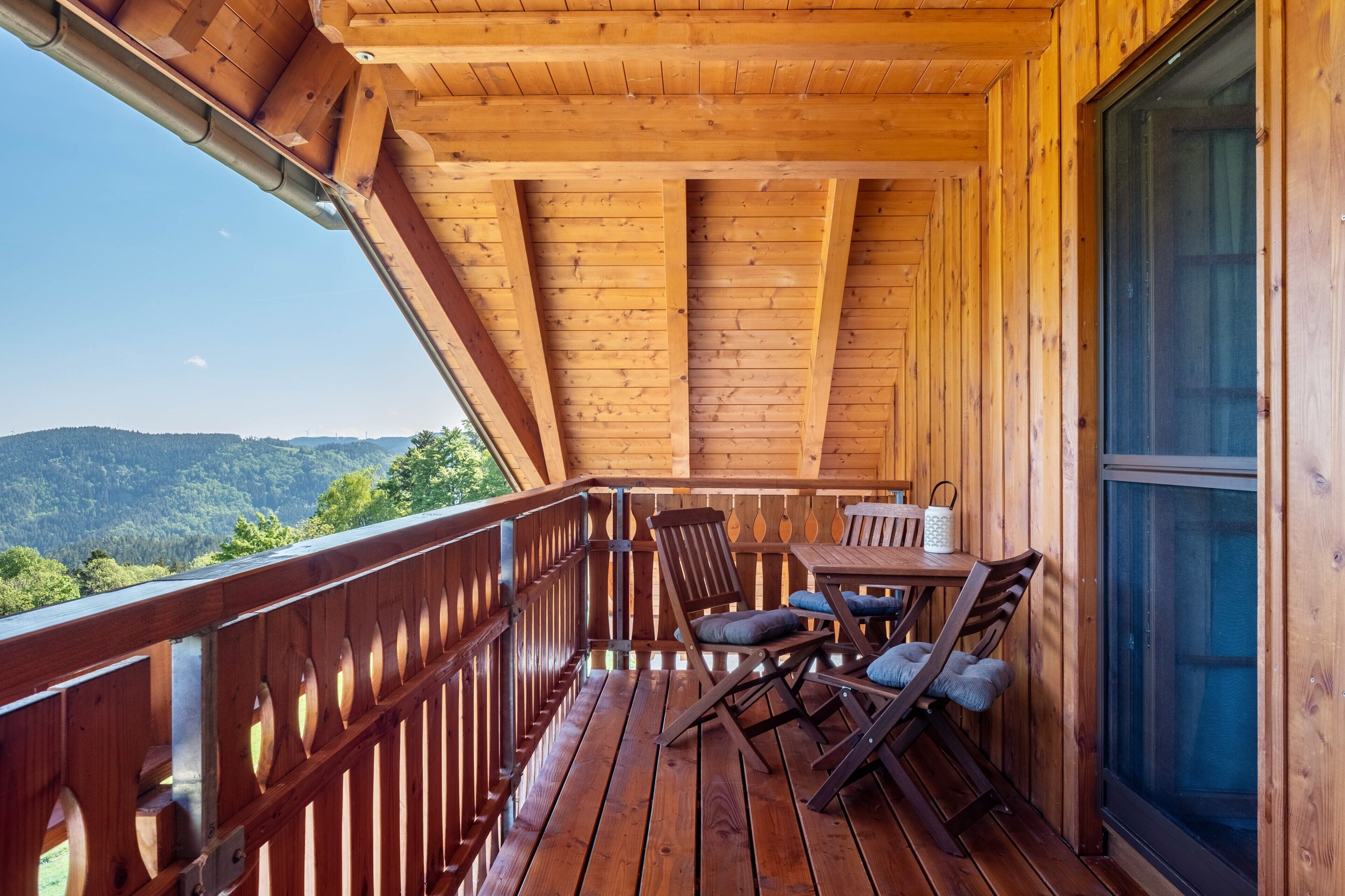 A wooden deck with a table and chairs, a railing, and a view of the mountains.