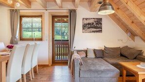 A cozy room with a wooden ceiling, a grey sofa, a dining table with chairs, and a view of a green landscape through a window. - Apartment 'Panoramic View, 85sqm' with Shared Terrace, Garden and Wi-Fi (Schonach)