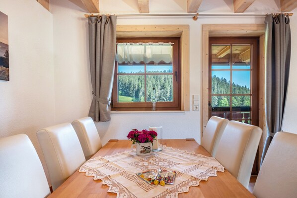 A dining area with a table set for four, a vase with flowers, and a window with a view of trees.