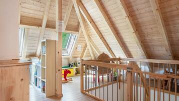 A high-ceilinged room with wooden beams, a crib, and a bookshelf.