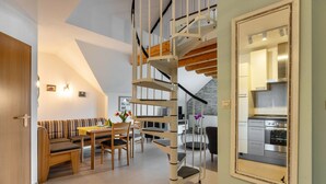 Un interior moderno con una escalera de caracol, una zona de comedor con una mesa y sillas de madera, y una cocina visible a través de un espejo.