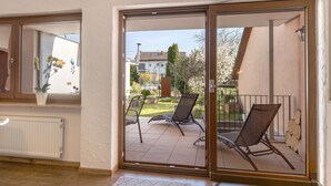 A room with a sliding glass door leading to an outdoor patio with two chairs and a small garden.