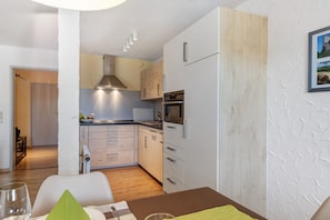 A modern kitchen with white cabinets, a built-in oven, and a dining area with a table and chairs.
