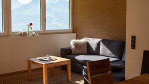 A living room with a sofa, a wooden table, and a window with a view of mountains. - Apartment 'Konzett Top 3' with Mountain View, Shared Terrace and Wi-Fi (Fontanella)