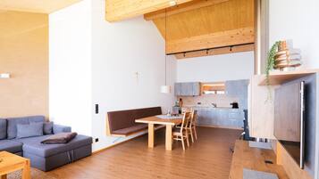 Et moderne interiør med træloft, spiseområde med bord og stole, en sofa og et køkken i baggrunden.