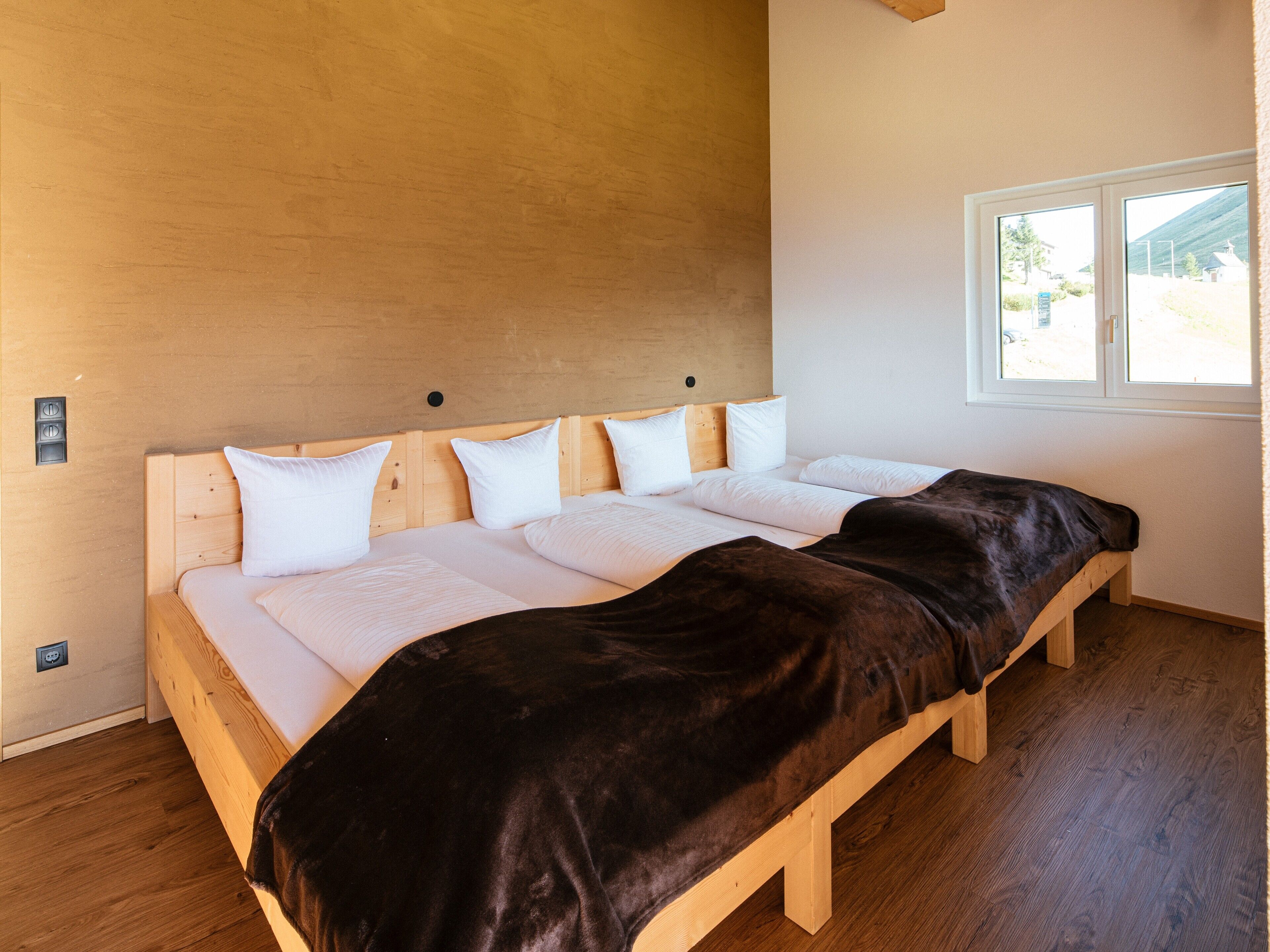A bedroom with a wooden bed, white bedding, a window, and a wooden floor.