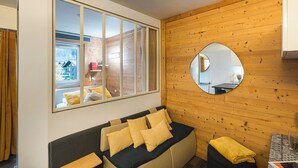 Une chambre moderne avec une grande fenêtre, un miroir rond et un canapé agrémenté de coussins.