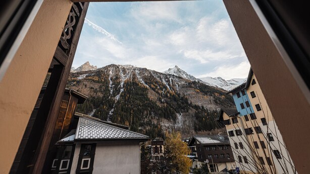 Une vue sur les montagnes, avec des sommets enneigés, une ville aux bâtiments traditionnels et un ciel dégagé.