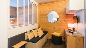 Une pièce chaleureuse avec un mur en bois, un miroir rond, un canapé avec des coussins, une petite table avec une lampe et une fenêtre.