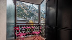 Un balcon donnant sur une chaîne de montagnes, deux chaises roses et une table.