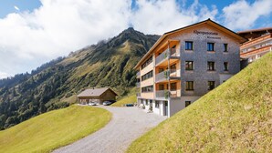Een meerhoog hotel met balkons, een berg op de achtergrond en een grindpad.