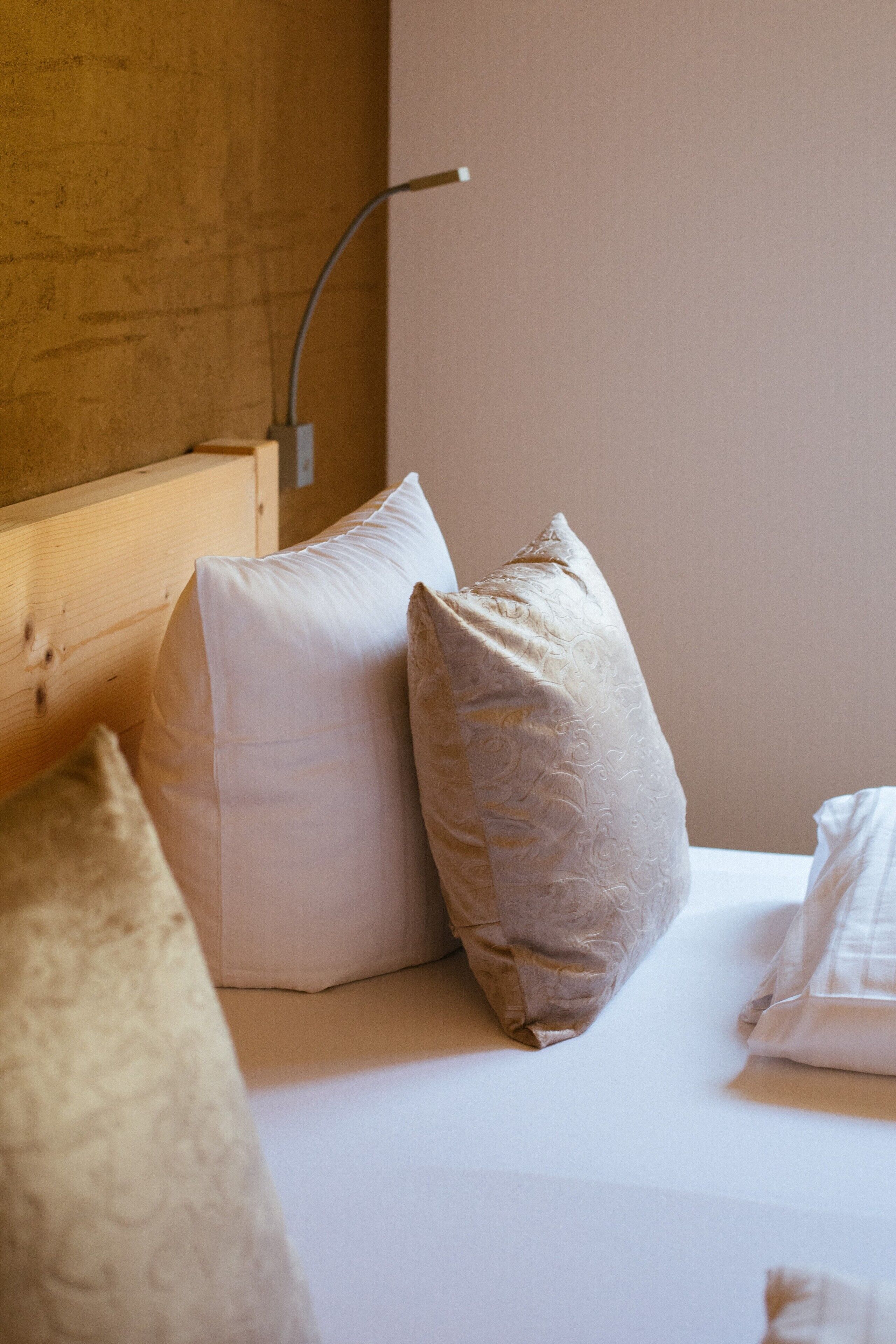 Una cama con ropa blanca y dos almohadas, cabecera de madera y lámpara fijada a la pared.