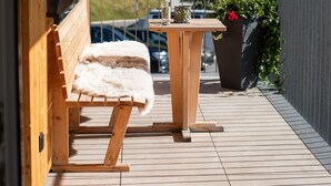 Een houten balkon met een bankje, een tafel en een bloempot.