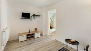 Een moderne woonkamer met een televisie, een houten kast, een klein tafeltje en een trap op de achtergrond.