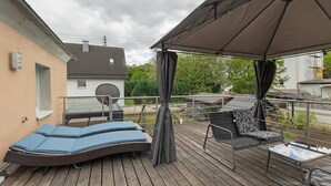 Een terras met een zonnescherm, lounge fauteuils en een tafel.