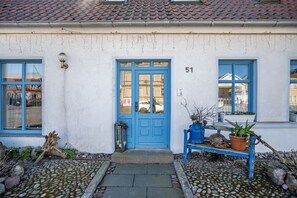 Un bâtiment avec une porte bleue, portant le numéro 51, et un banc agrémenté de plantes en pot, situé à l’extérieur.