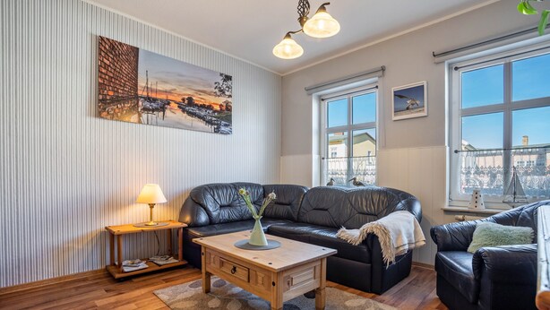 A living room with a black leather sofa, a wooden coffee table, a lamp, and a view of the city through large windows. - Holiday Apartment 'Blütenzauber' with Wi-Fi (Sagard)
