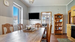 A dining area with a wooden table, chairs, a television, and a bookshelf. - Holiday Apartment 'Blütenzauber' with Wi-Fi (Sagard)