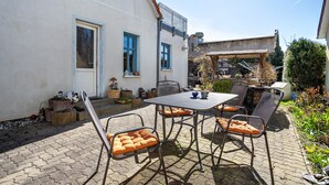 An outdoor patio with a table and chairs, a small garden area, and a building with a white exterior and blue windows. - Holiday Apartment 'Blütenzauber' with Wi-Fi (Sagard)