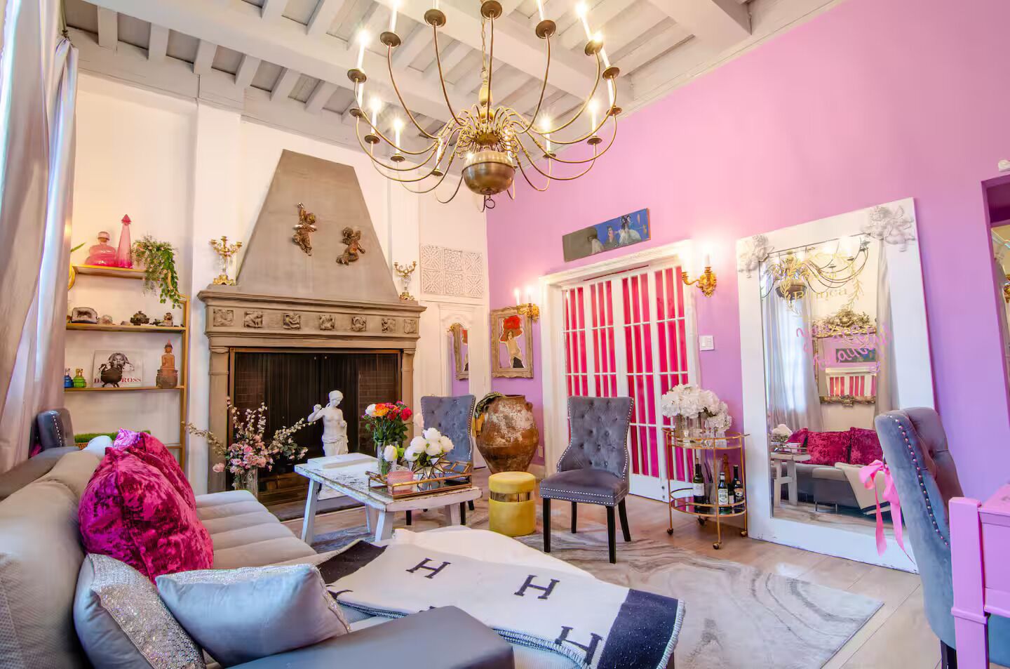 Een woonkamer met een open haard, een kroonluchter en een roze muur.
