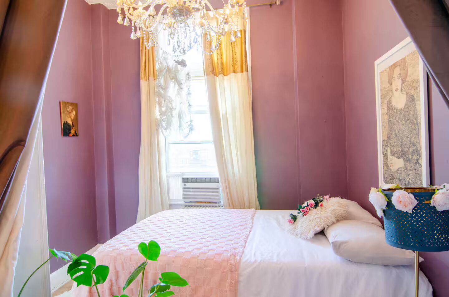 Un dormitorio con cama, ventana con cortinas, candelabro y un cuadro en la pared.