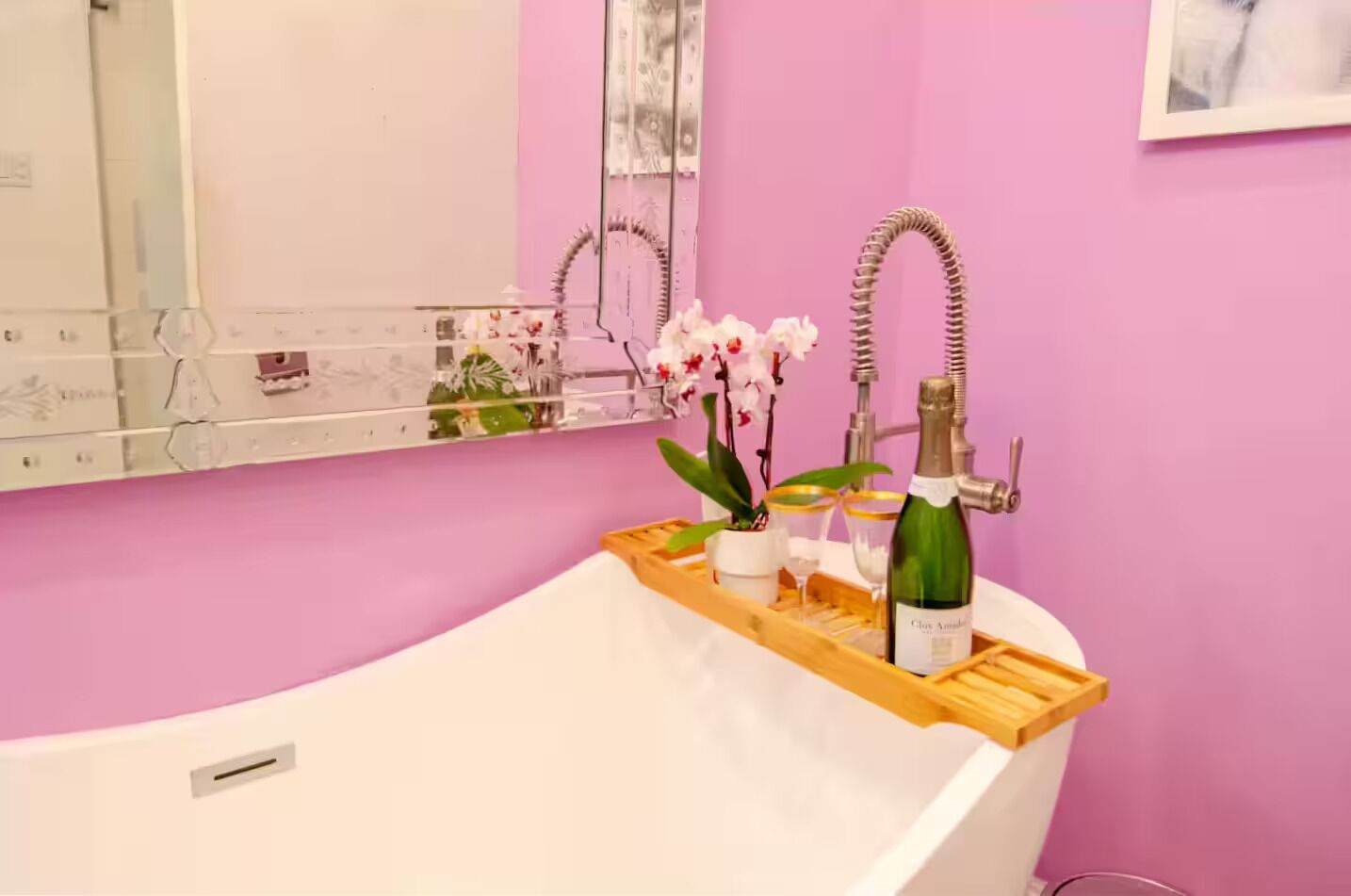 Een moderne badkamer met een vrijstaand bad, een wastafel met spiegel, en een houten dienblad met een fles champagne, een glas en een potorkidee.