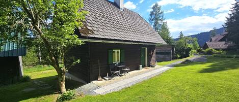 Ett rustikt trähus med ett sluttande tak, en skorsten och en liten veranda med utomhusmöbler.
