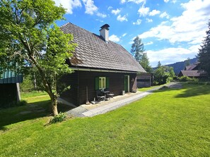 A rustic wooden house with a sloped roof, a chimney, and a small porch with outdoor seating.