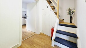 Una escalera con escalones de madera y alfombra azul, que conduce a una habitación con paredes blancas y techo de madera.