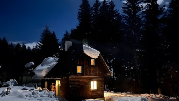 Una cabaña de madera con techo nevado, rodeada de árboles y un paisaje invernal.