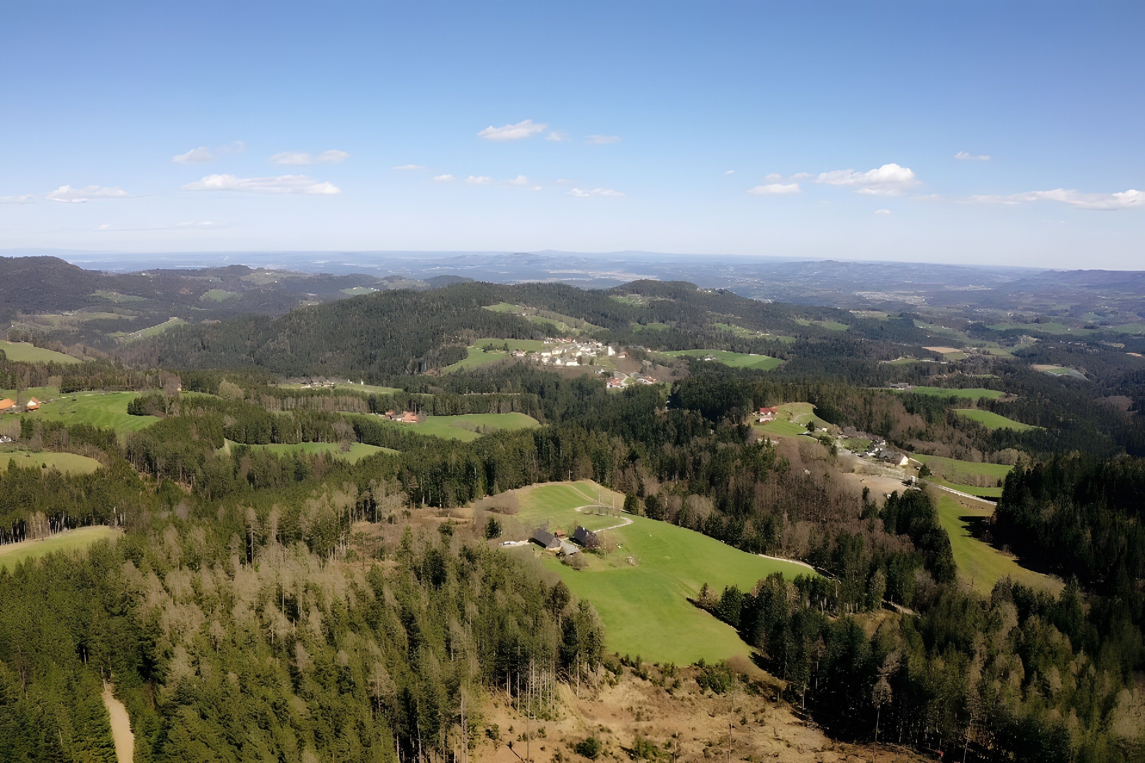 Laaja näkymä maaseutumaisemaan, jossa on kumpuilevia kukkuloita, harvakseltaan sijaitsevia taloja ja tiheää metsää.