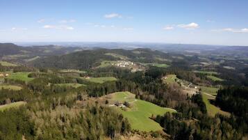 Un panorama sur un paysage rural, avec des collines ondoyantes, des maisons dispersées et de vastes forêts.