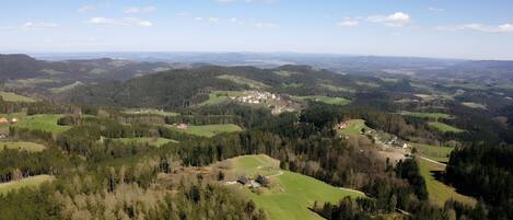 Laaja näkymä maaseutumaisemaan, jossa on kumpuilevia kukkuloita, harvakseltaan sijaitsevia taloja ja tiheää metsää.