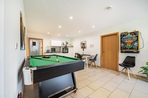 Una mesa de billar en una habitación con cocina, zona de comedor y una puerta.