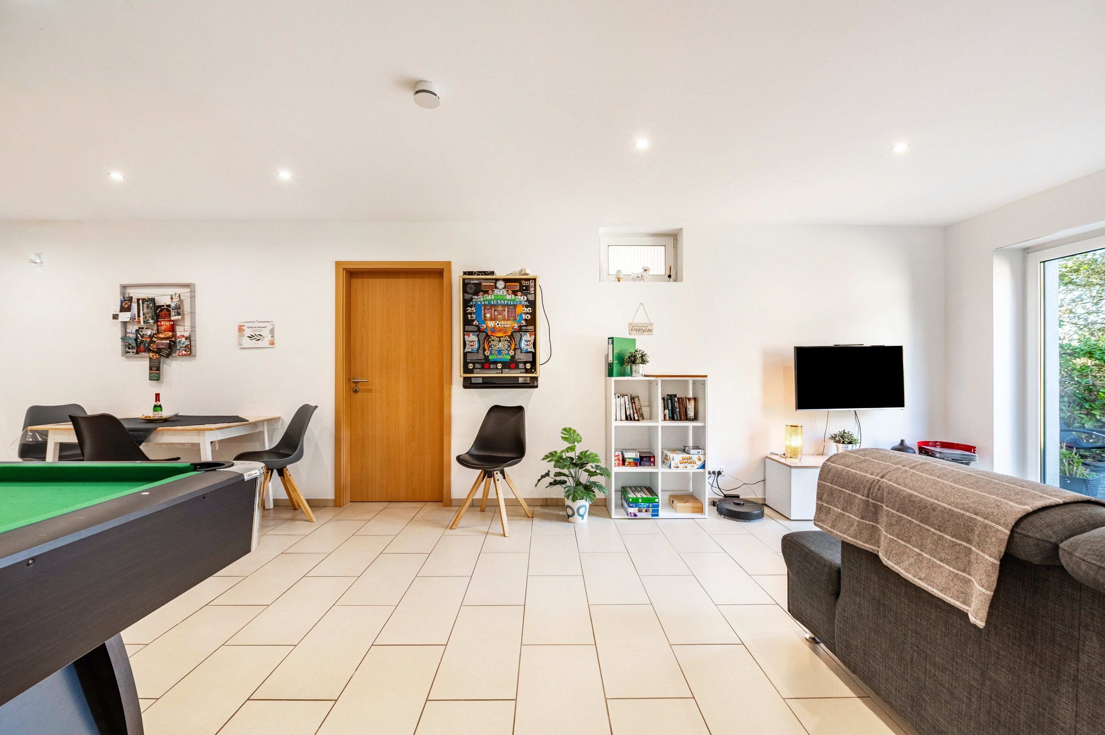 A modern living room with a pool table, a sofa, a television, and a bookshelf.