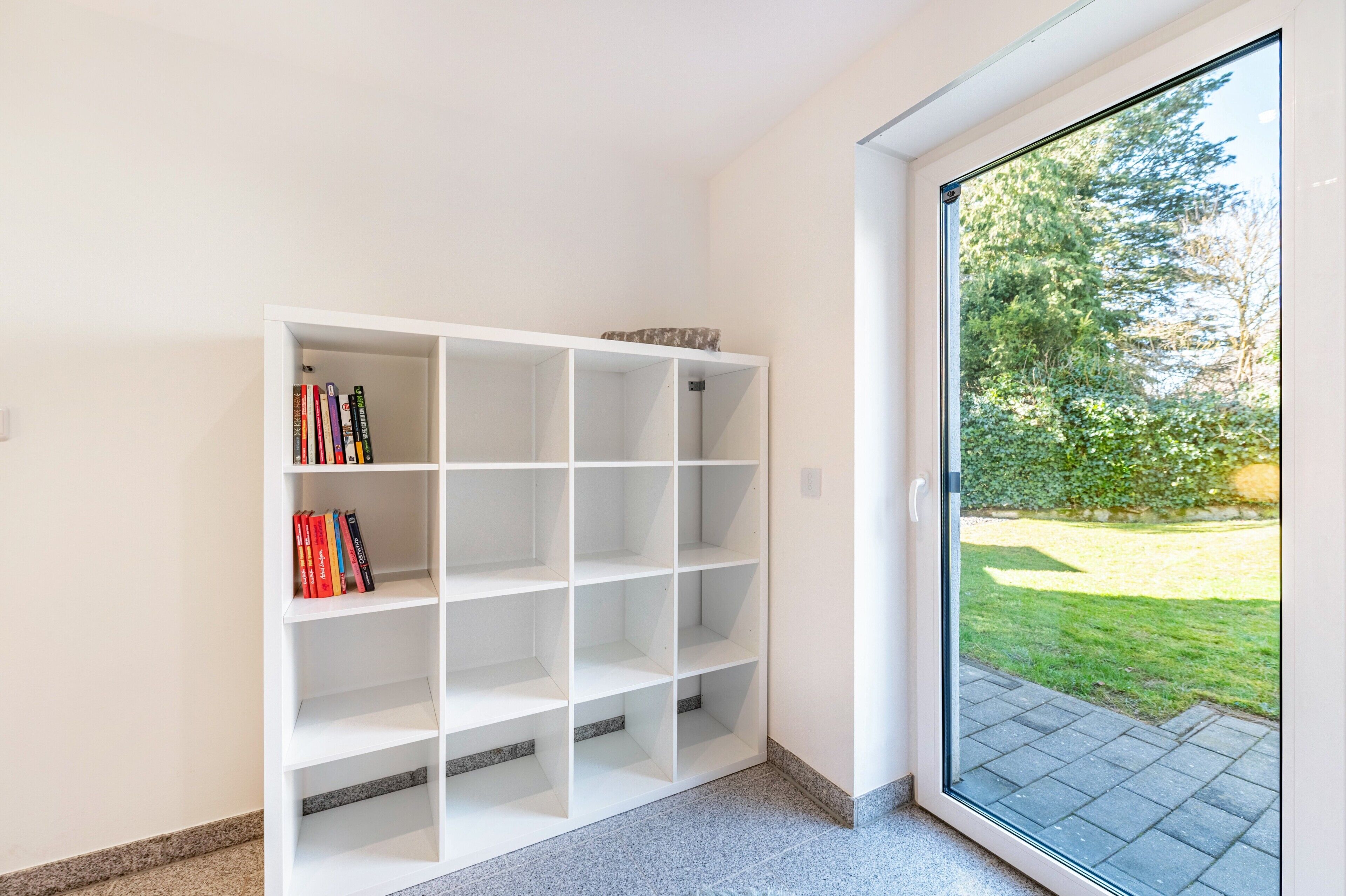 Una libreria bianca con libri, e una porta in vetro che dà su un giardino.