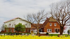 A two-story house with a red brick facade, a white upper section, and a white picket fence. - Apartment 'Norderoog' with Private Terrace, Shared Garden and Wi-Fi (Nordstrand)