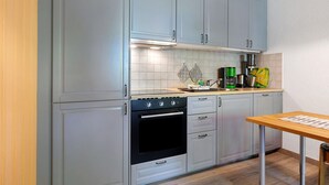 A kitchen with light blue cabinets, a black oven, a wooden table, and a tiled backsplash. - Apartment 'Norderoog' with Private Terrace, Shared Garden and Wi-Fi (Nordstrand)