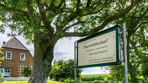 A signboard with text in a foreign language, a tree, and a brick building in the background. - Apartment 'Norderoog' with Private Terrace, Shared Garden and Wi-Fi (Nordstrand)