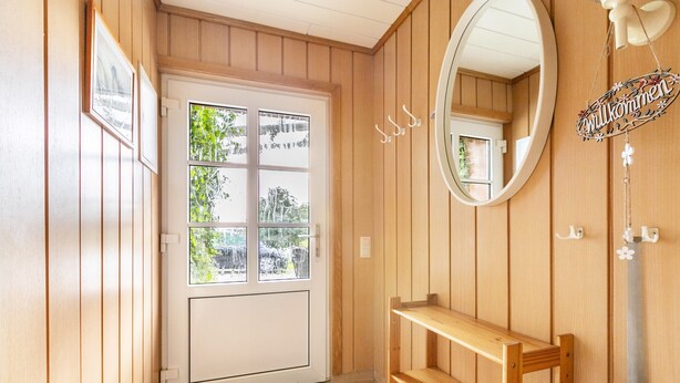 Un intérieur en bois avec une porte blanche, un miroir et une pancarte de bienvenue.
